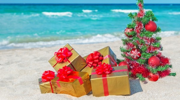 Christmas tree and golden gift with big red bow on the sea beach