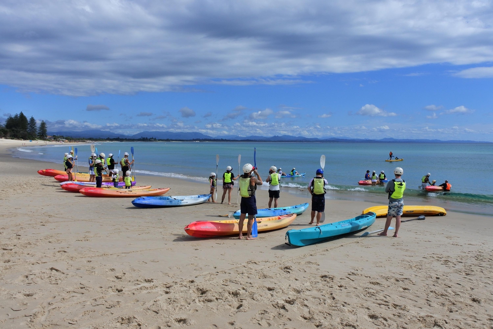 BYRON BAY, NSW - APR 02 2023: Large group of Australian people learn how to use kayak in Byron Bay beach. Kayak is a small, narrow human-powered watercraft that has been used for at least 4,000 years.